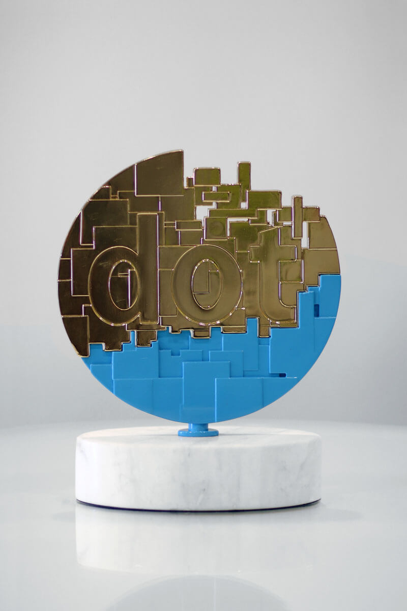 The gold dotCOMM Award is a metal cast dot broken up into individual bits. The 3-D dot sits above an oblong marble base. The gold dotCOMM Award is a metal cast dot broken up into individual bits. The 3-D dot sits above an oblong marble base.