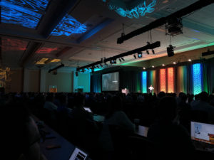 Photo of audience with keynote speaker during the conference in a dim setting